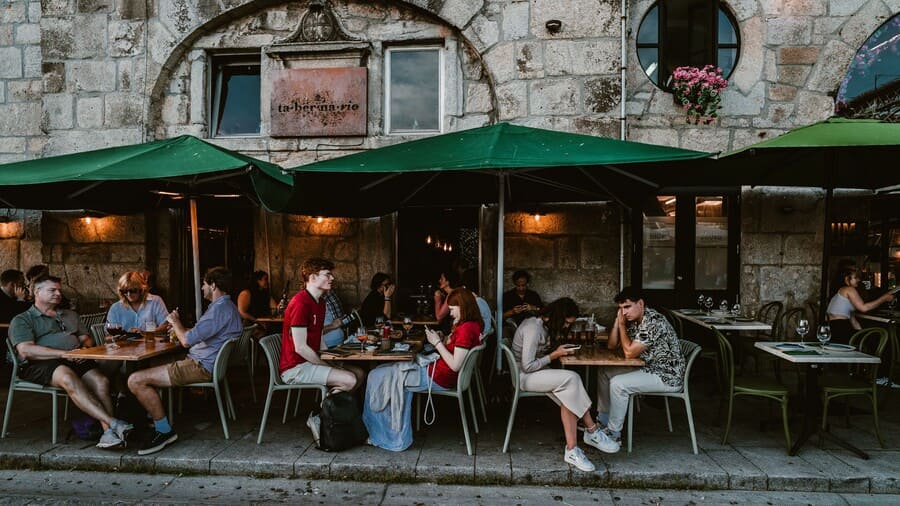 Cafégasten zitten buiten onder de zonwering.